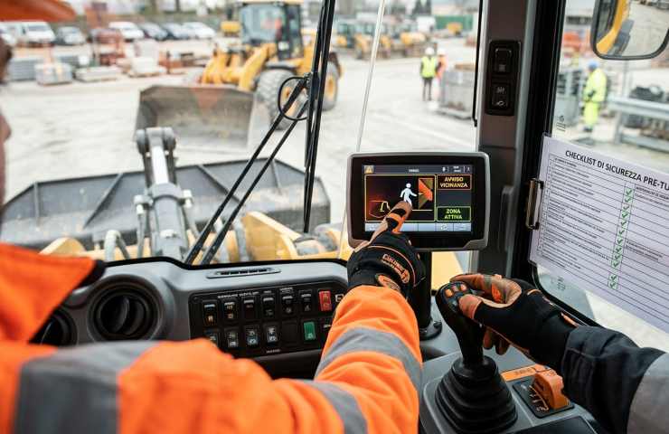 Console di controllo di una pala meccanica con display di sicurezza attivo e checklist per la prevenzione infortuni.