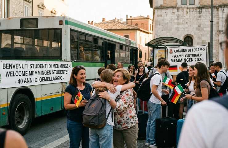 Accoglienza a Teramo di studenti tedeschi da Memmingen per scambi culturali del 40° anniversario gemellaggio: abbraccio tra madre ospitante teramana e studentessa, con cartello di benvenuto del Comune.