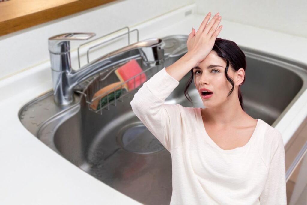 donna che si mette una mano in fronte e lavello della cucina