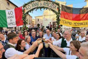Accoglienza a Teramo di studenti tedeschi da Memmingen per scambi culturali del 40° anniversario gemellaggio: abbraccio tra madre ospitante teramana e studentessa, con cartello di benvenuto del Comune.