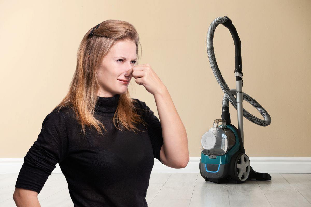donna che si tappa il naso per il cattivo odore che esce dall'aspirapolvere