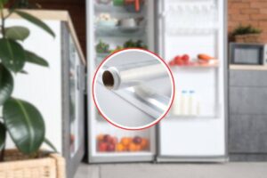 in primo piano due rotoli di pellicola trasparente e come sfondo una cucina con un frigo aperto